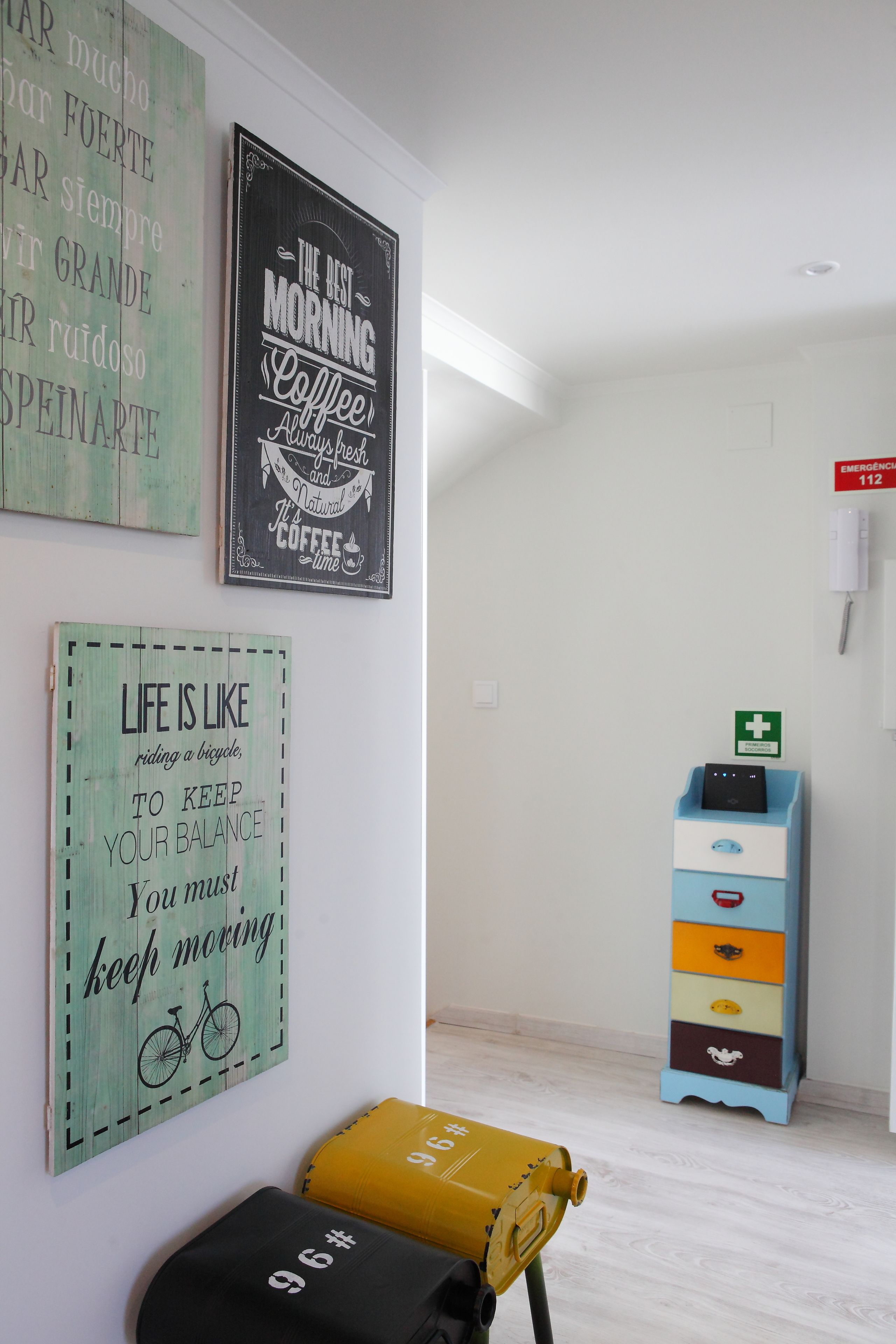 Une pièce dont un mur est décoré de citations inspirantes, avec une armoire bleue dotée de tiroirs et un sac jaune posé sur le sol.
