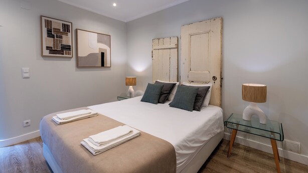 Quarto com cama grande, duas mesas de cabeceira, espelho fixado na parede e porta com acabamento rústico.