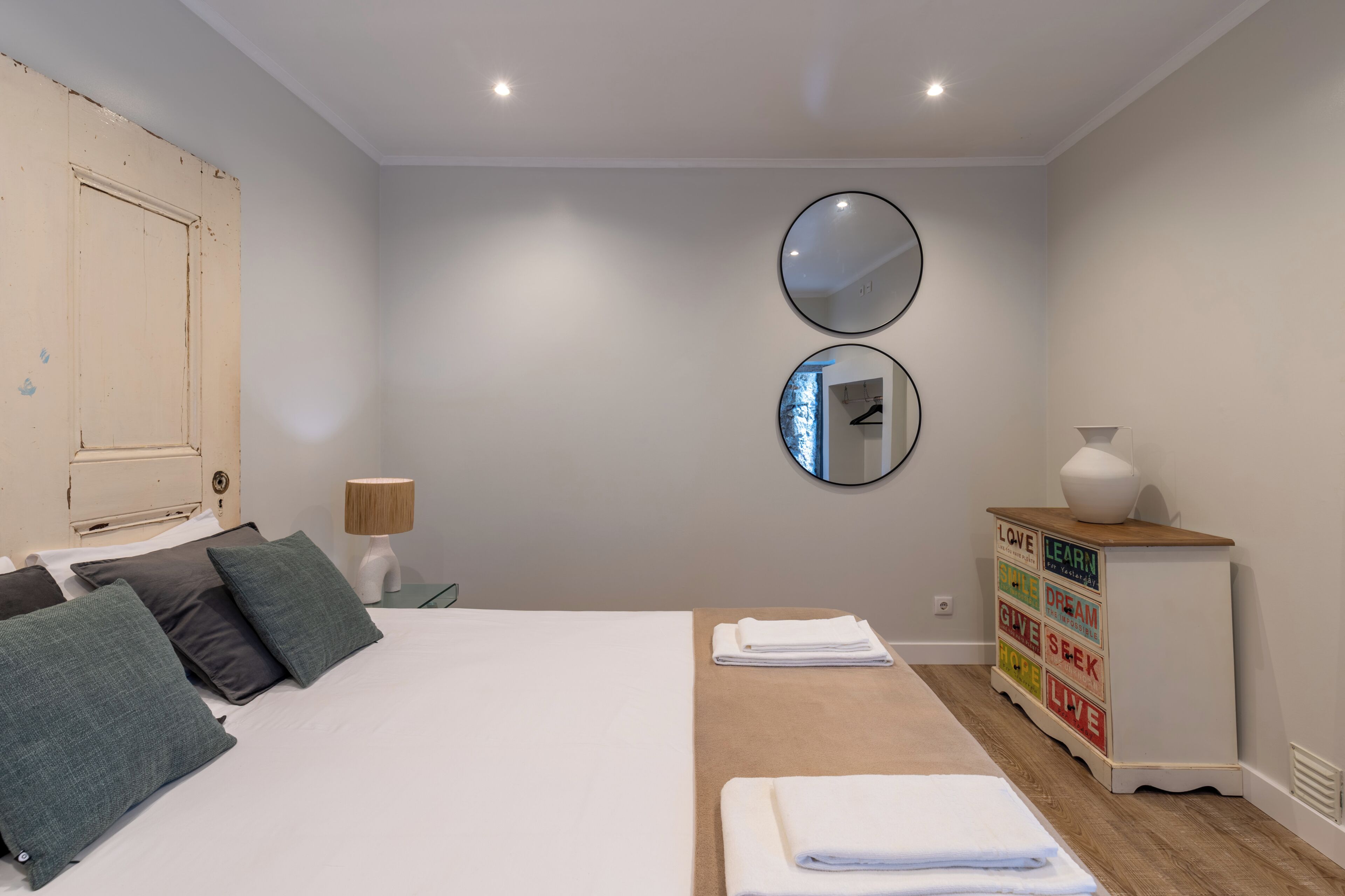 Un dormitorio con cama, dos espejos en la pared, un aparador con palabras motivacionales y una lámpara de noche.