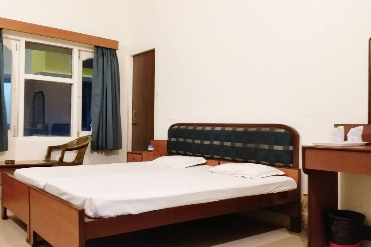 A bedroom with a wooden bed, a desk, a chair, and a window with curtains.