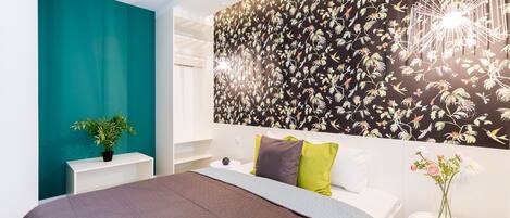 Ein modernes Schlafzimmer mit einem großen Bett, einer Wand in Türkis, floralem Wandpapier und einem kleinen Tisch mit einem Blumenvasen.