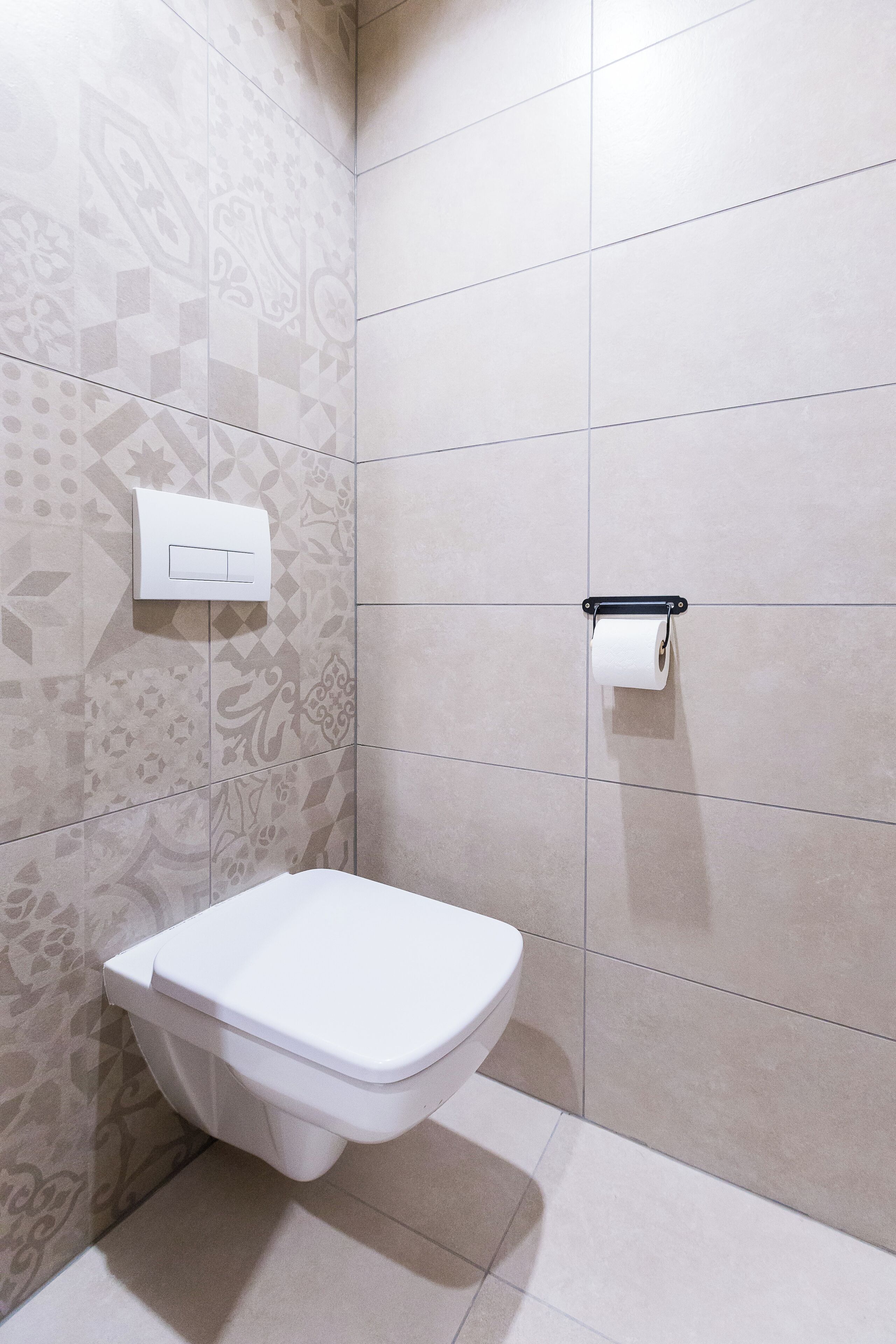 A bathroom with a toilet, a toilet paper holder, and patterned tiles on the walls.