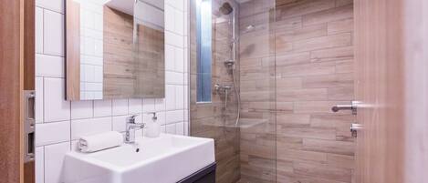 Un baño moderno con cabina de ducha de vidrio, un lavabo blanco y un espejo encima.