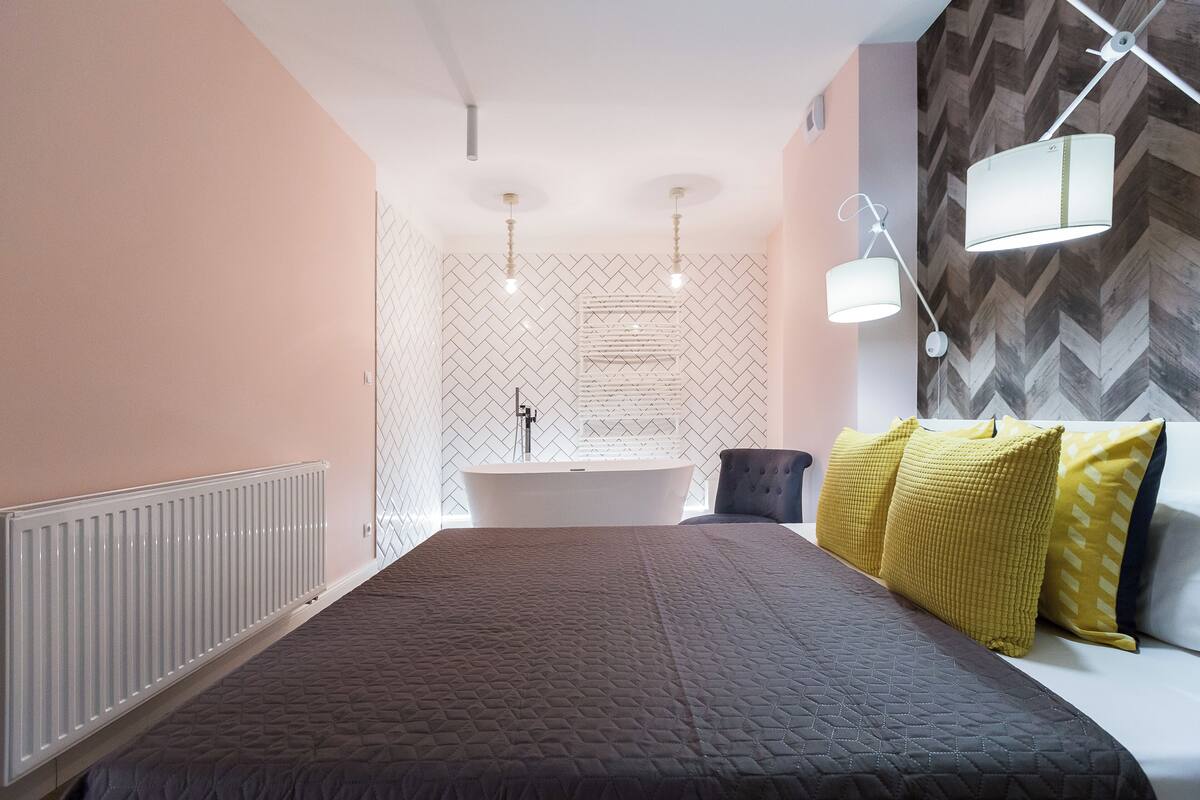 Ein modernes Schlafzimmer mit einem großen Bett, einer eingebauten Badewanne und einer Wand mit einem einzigartigen Fischgrätmuster.
