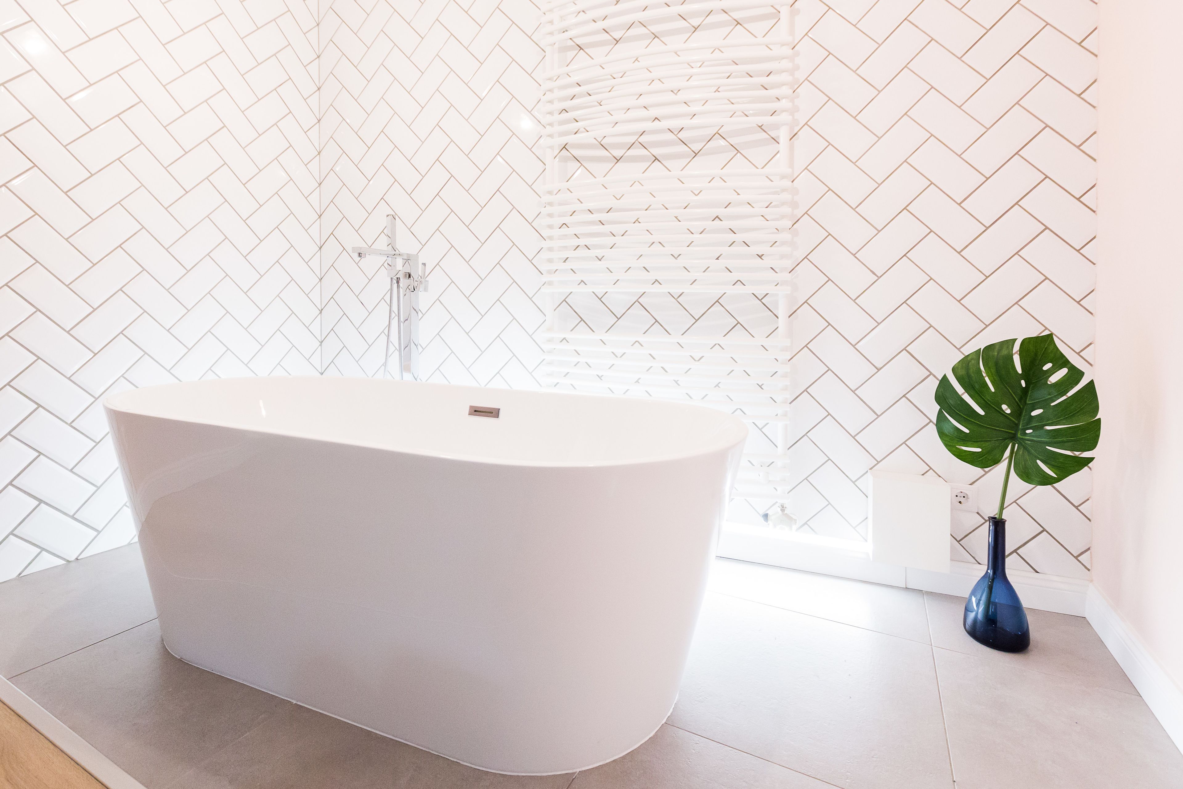 Un baño moderno con una bañera independiente, una planta en maceta y un revestimiento de pared con motivo de espiga.