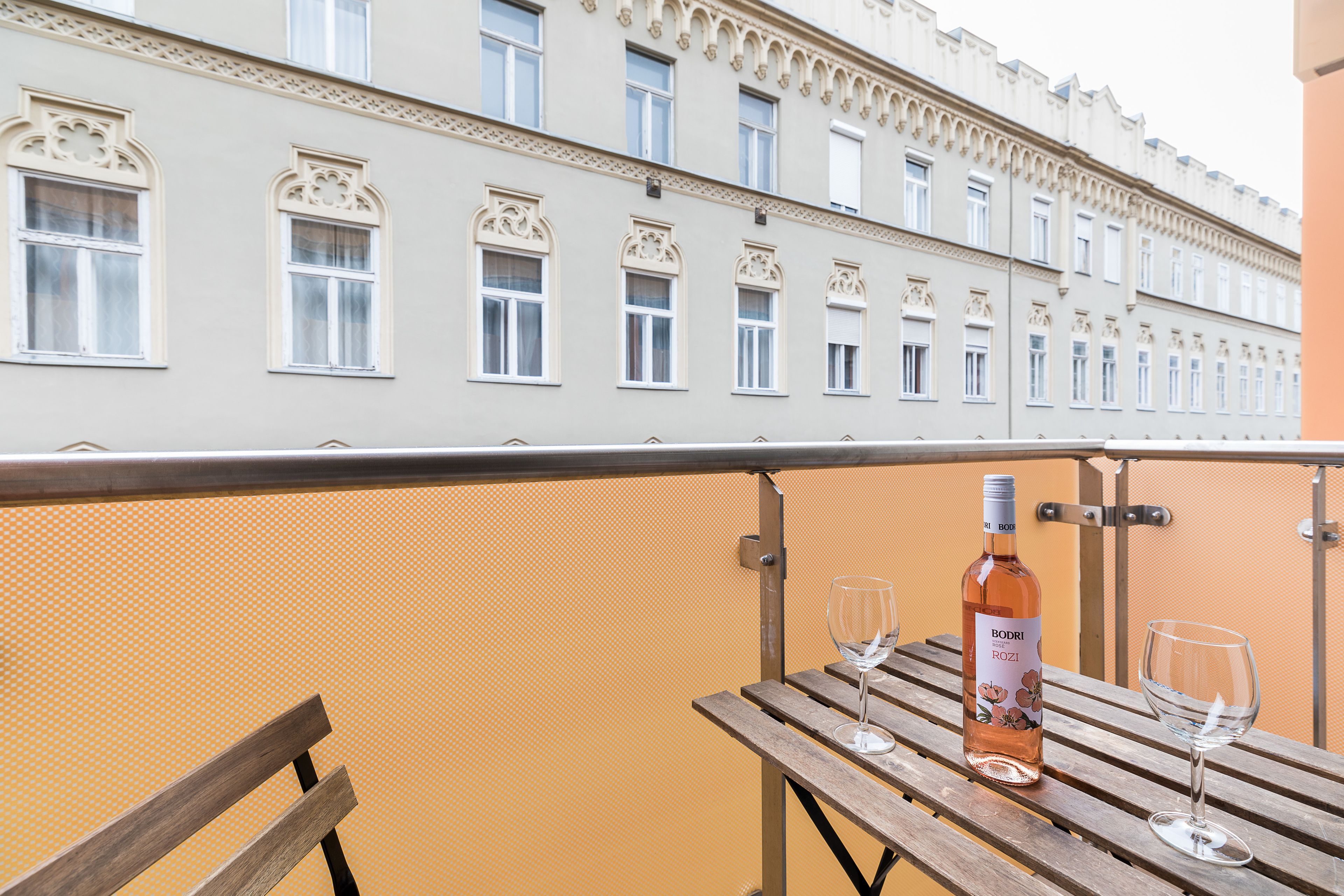 A balcony with a wooden table, a bottle of wine, and two glasses.