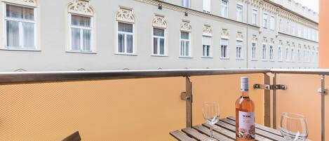 A balcony with a wooden table, a bottle of wine, and two glasses.