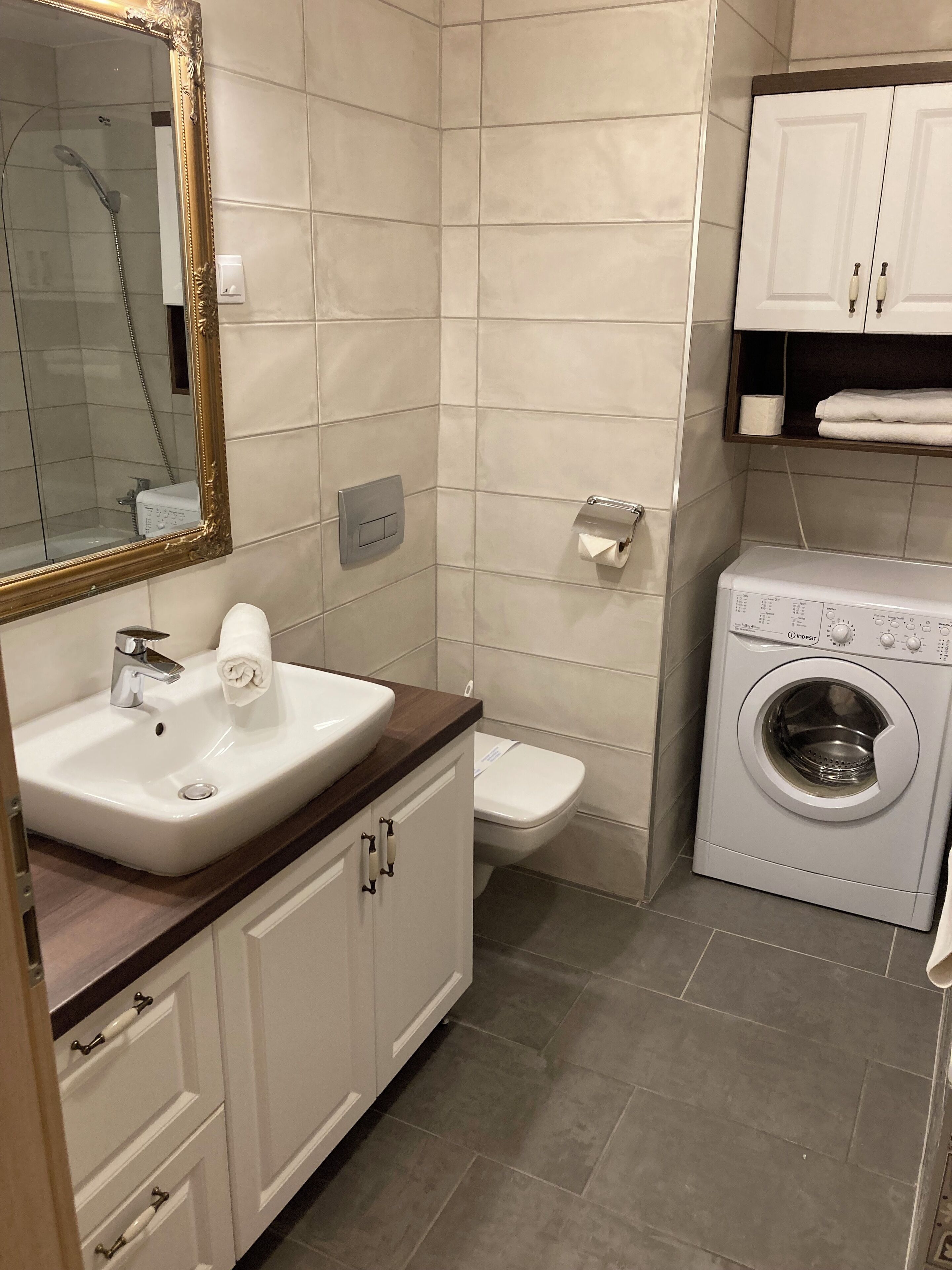 A bathroom with a sink, mirror, toilet, and washing machine.