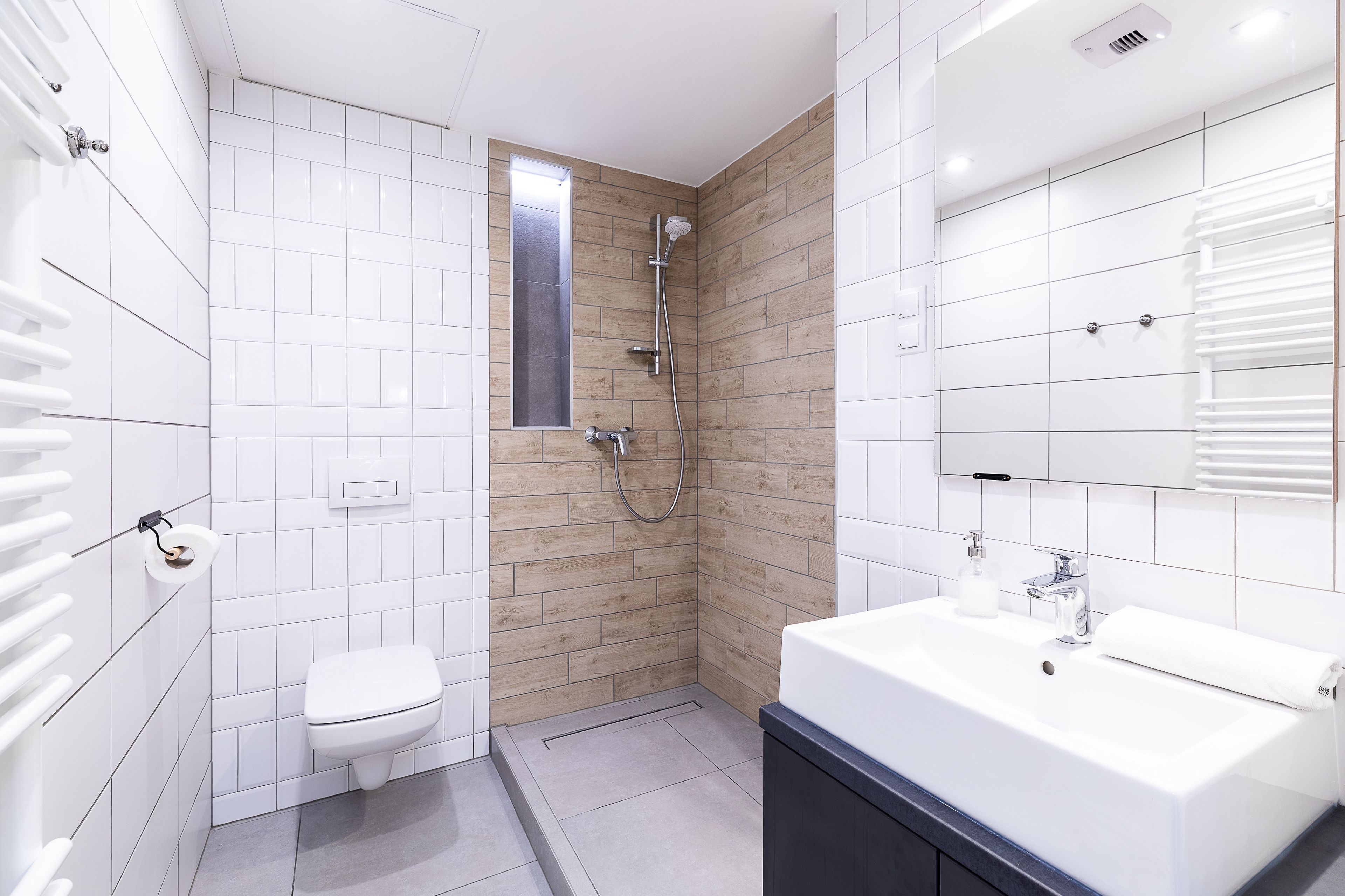 A modern bathroom with a white toilet, a shower with a wooden accent wall, and a large sink with a mirror.