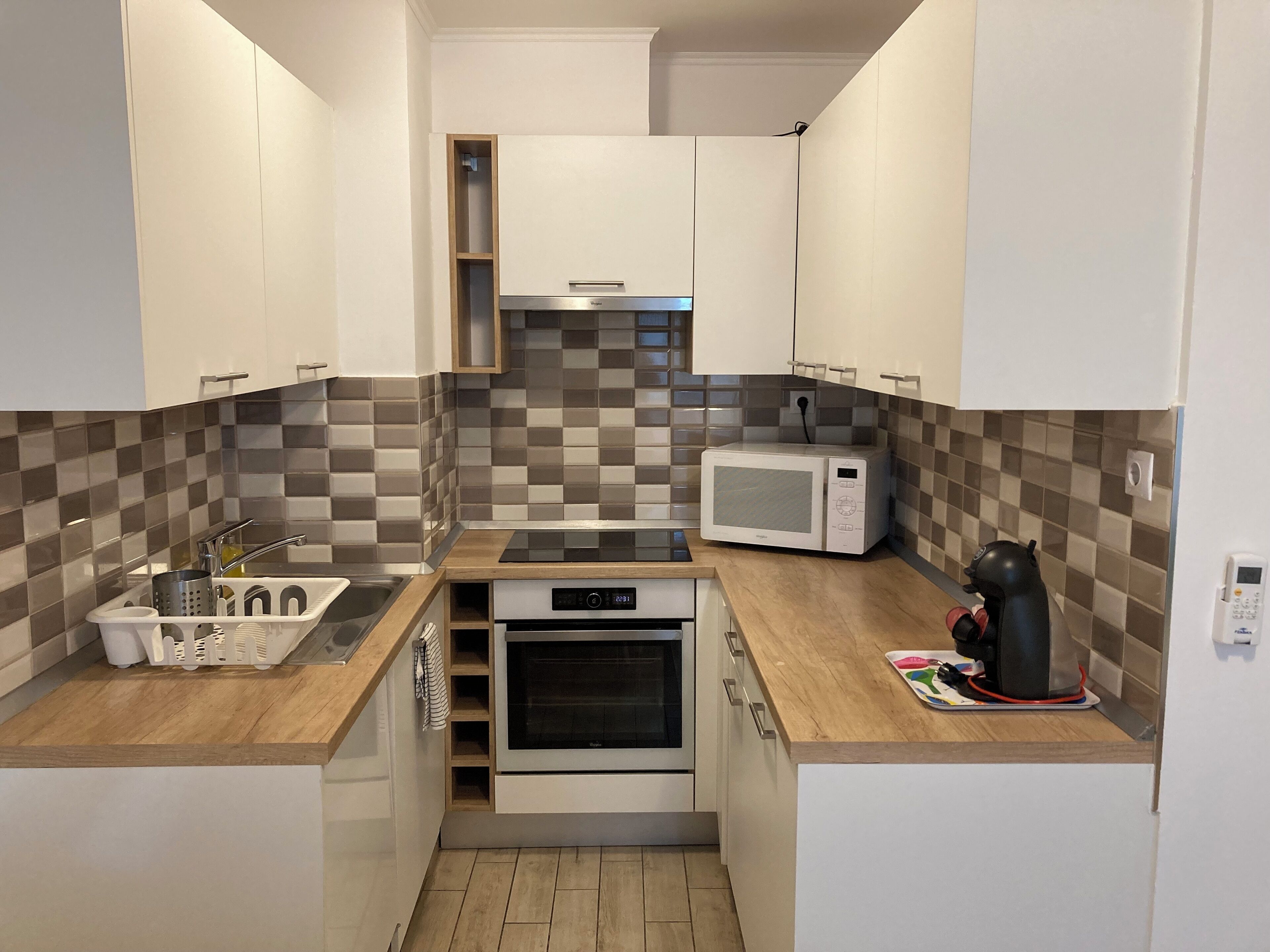 Una cucina compatta con mobili bianchi, un forno a microonde, un bollitore e una lavastoviglie.