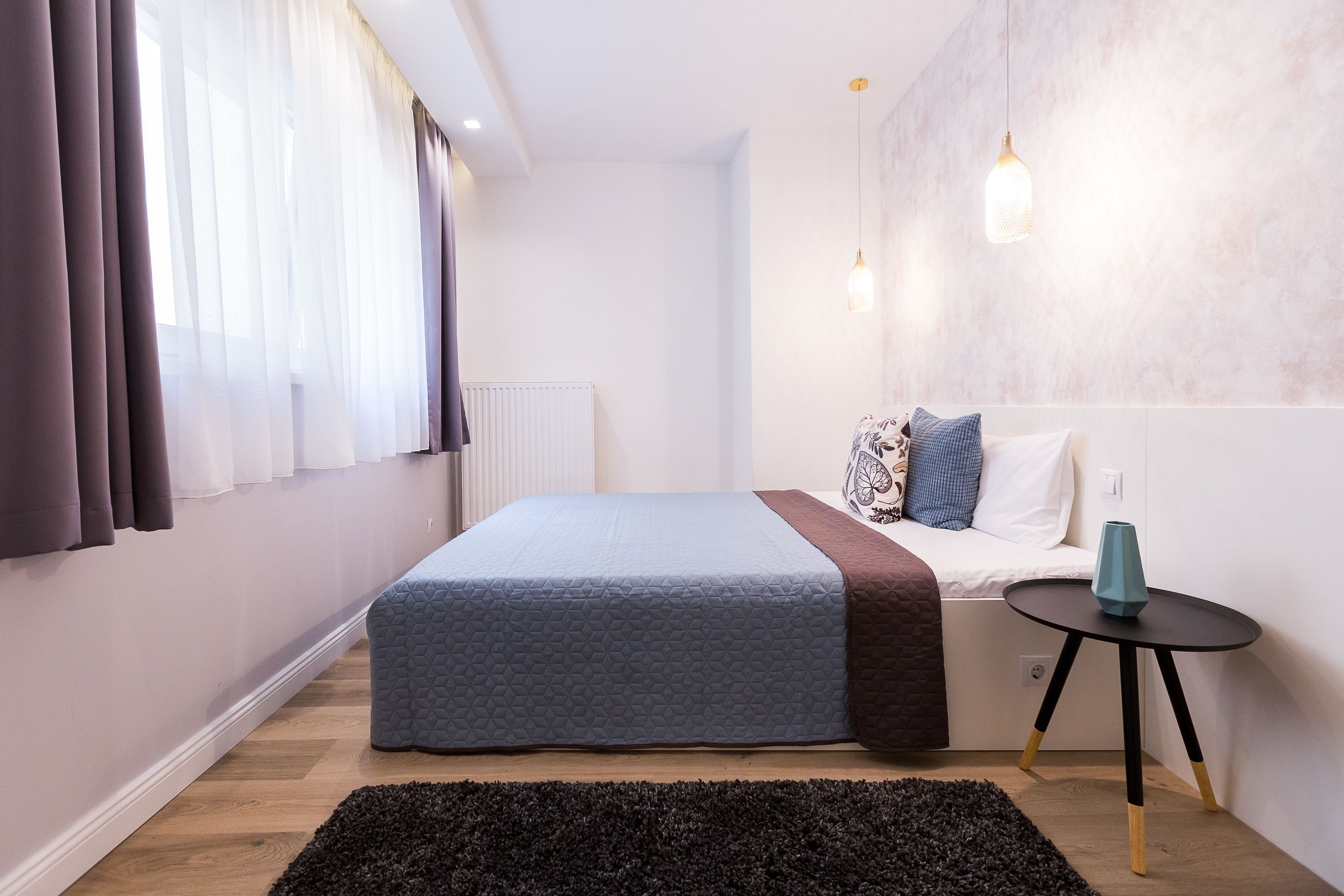 A bedroom with a bed, bedside table, and a wall-mounted light fixture.