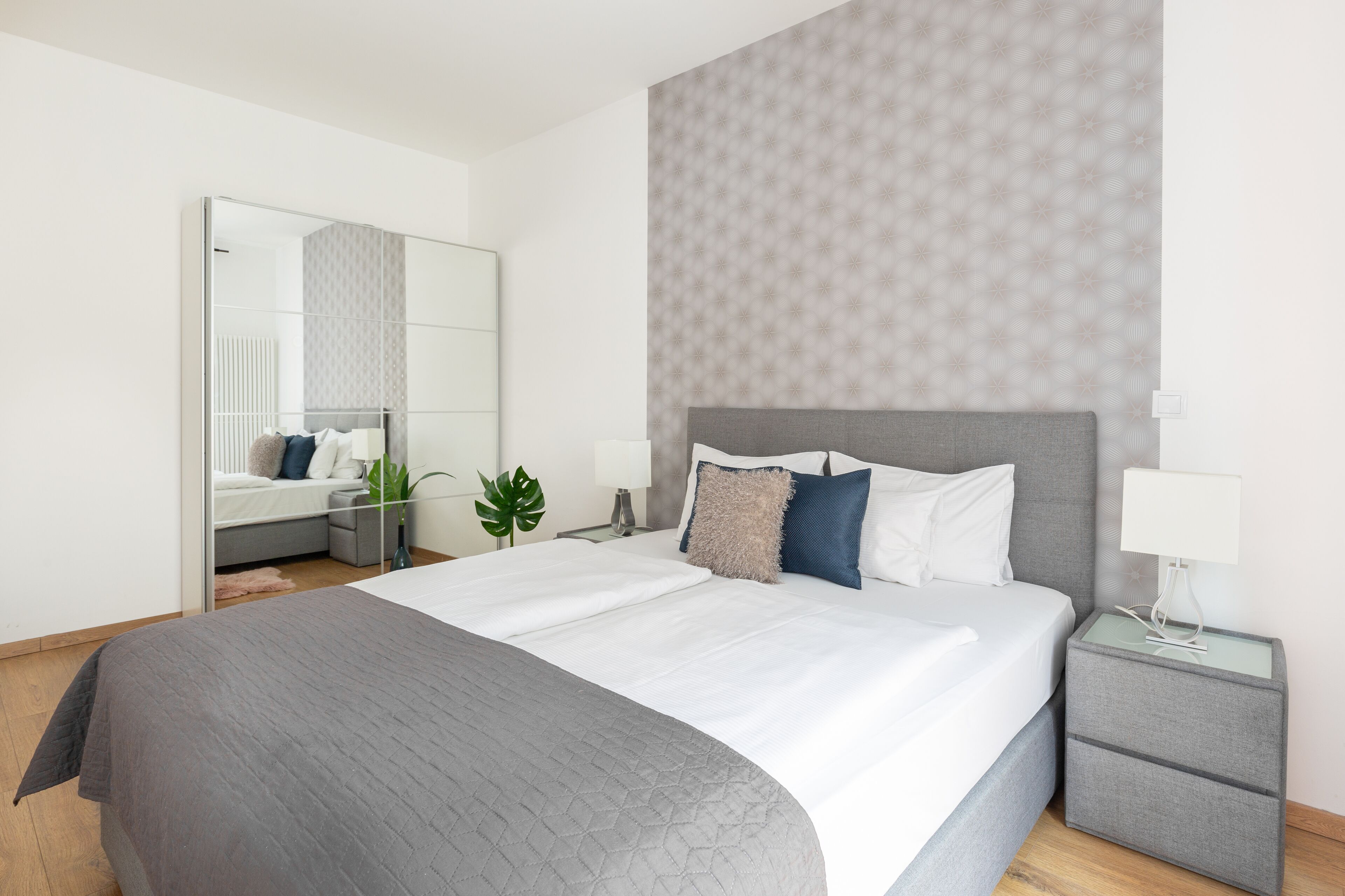 A modern hotel room with a large bed, a bedside table, a nightstand, and a mirror.