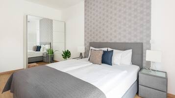 A modern hotel room with a large bed, a bedside table, a nightstand, and a mirror.