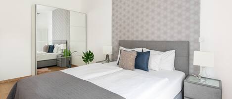 A modern hotel room with a large bed, a bedside table, a nightstand, and a mirror.
