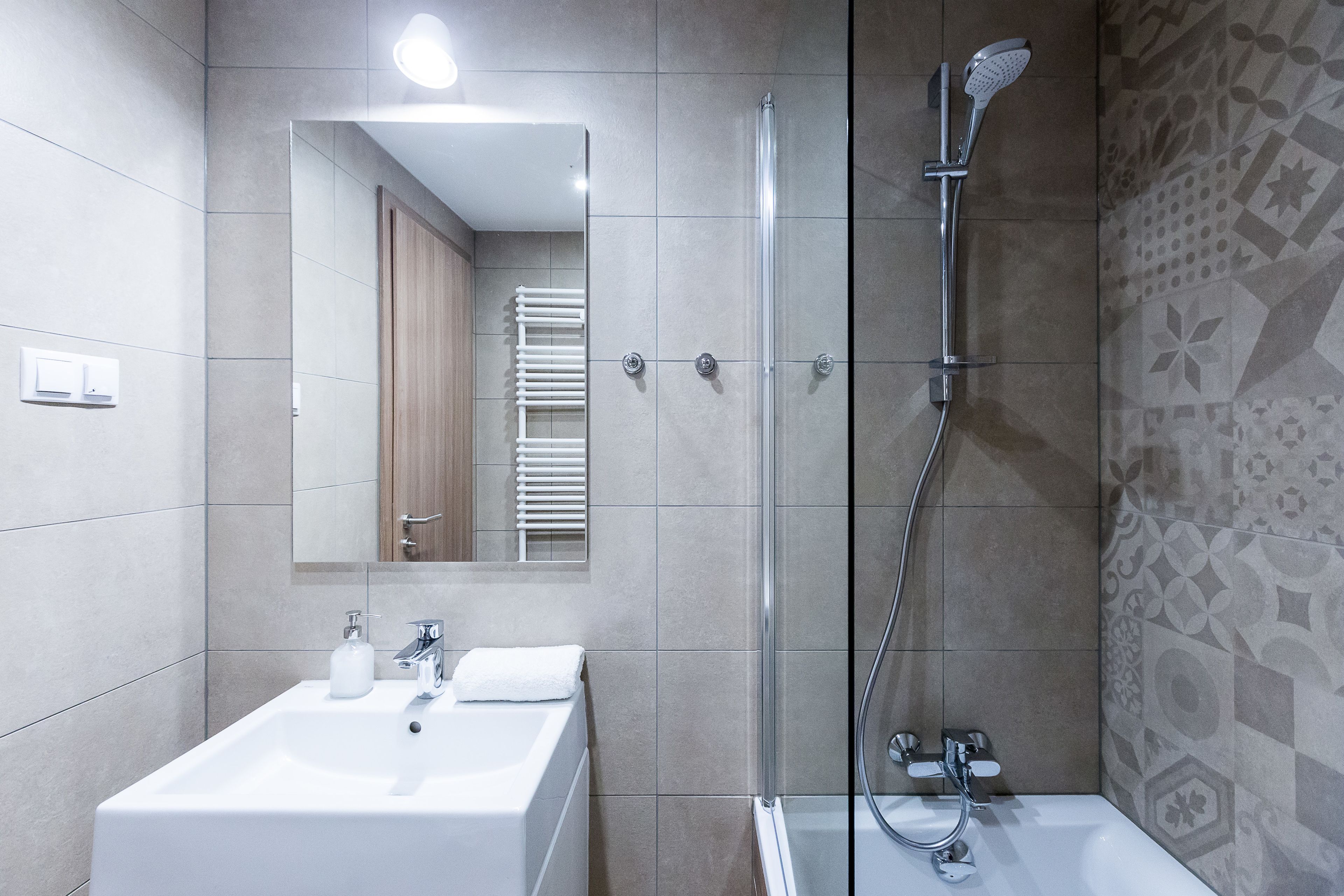 A modern bathroom with a glass-enclosed shower, a white sink, and a mirror above it.