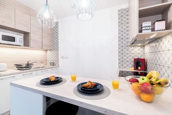 A modern kitchen with a microwave, a fruit bowl, and a croissant on a plate.