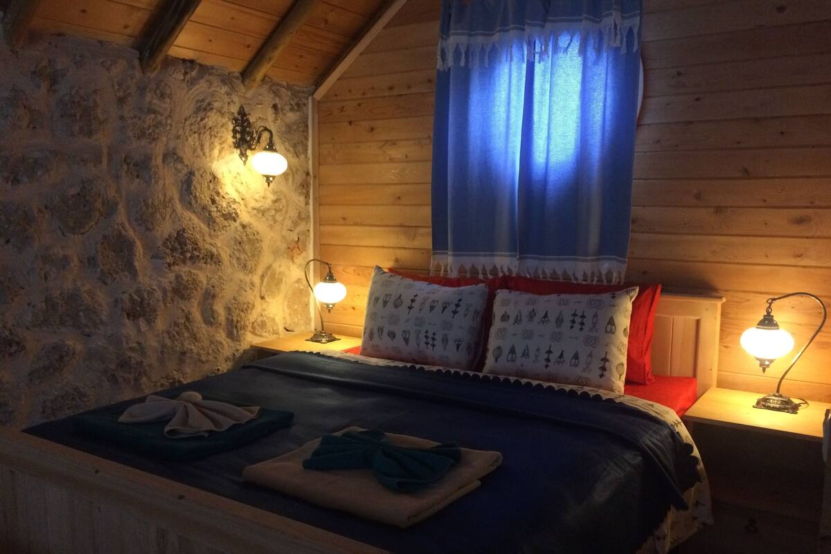 A cozy room with a wooden bed, two bedside lamps, and a stone wall.