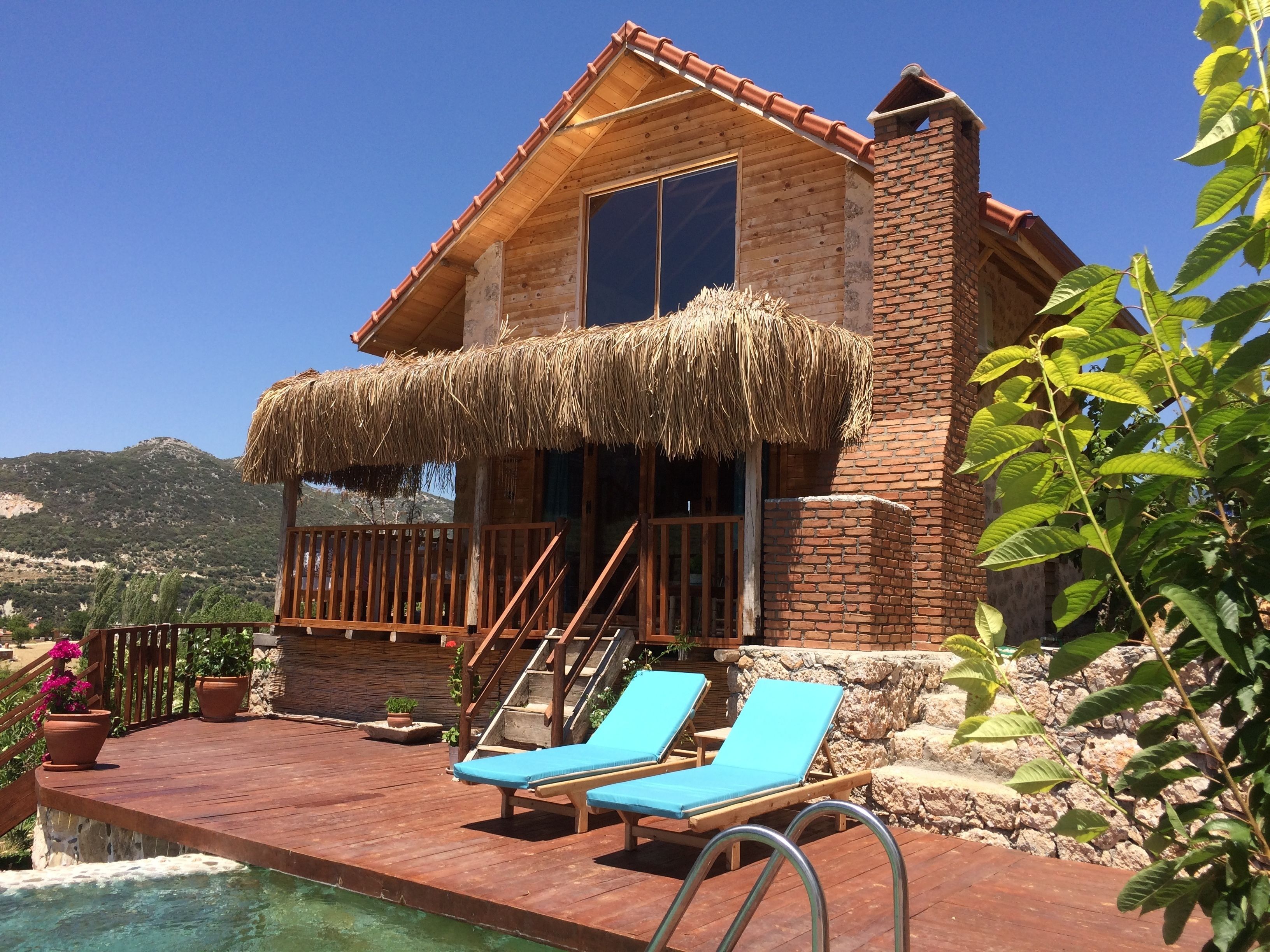 Una casa de madera con techo de paja, una piscina y dos sillones azules.