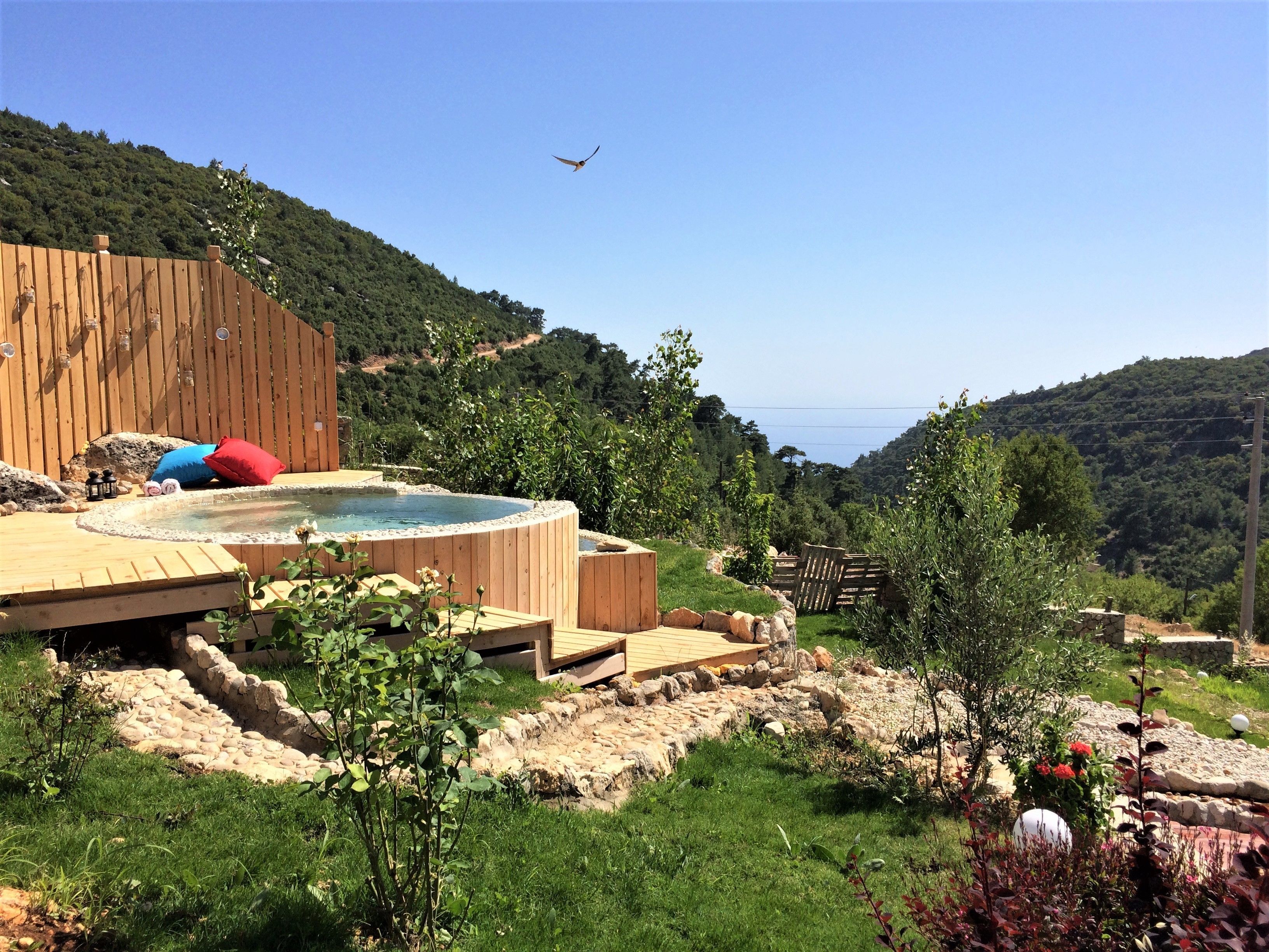 A hot tub area with wooden decking, a stone wall, and a view of a mountainous landscape.