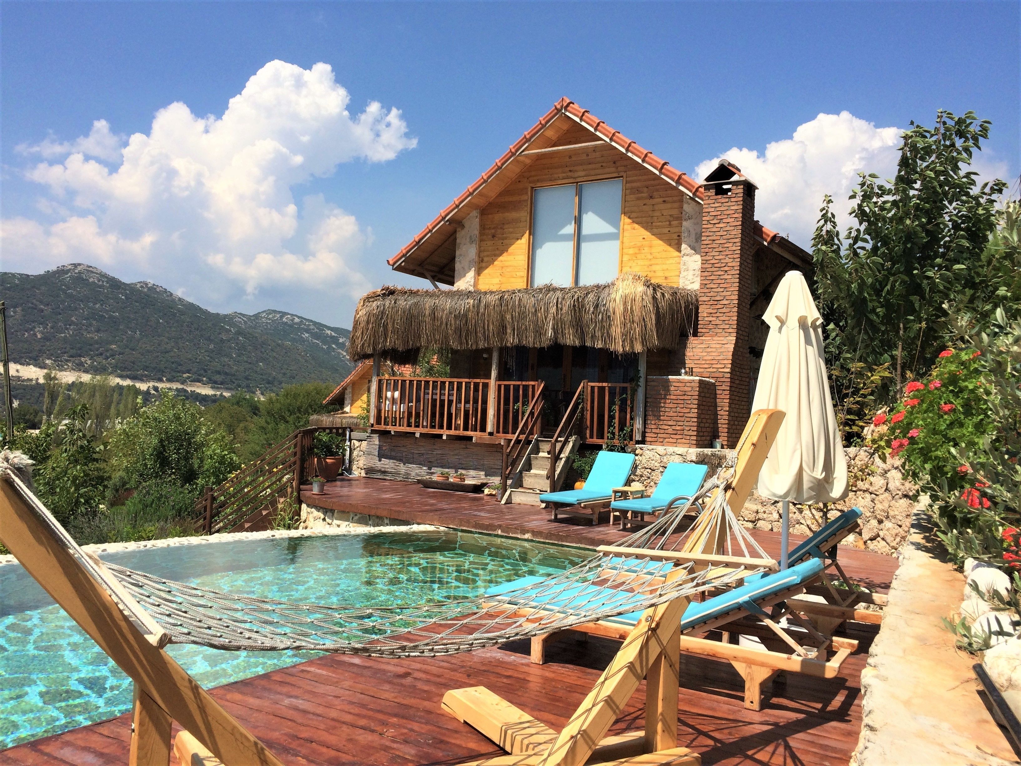A wooden villa with a pool, blue lounge chairs, and a thatched roof balcony.