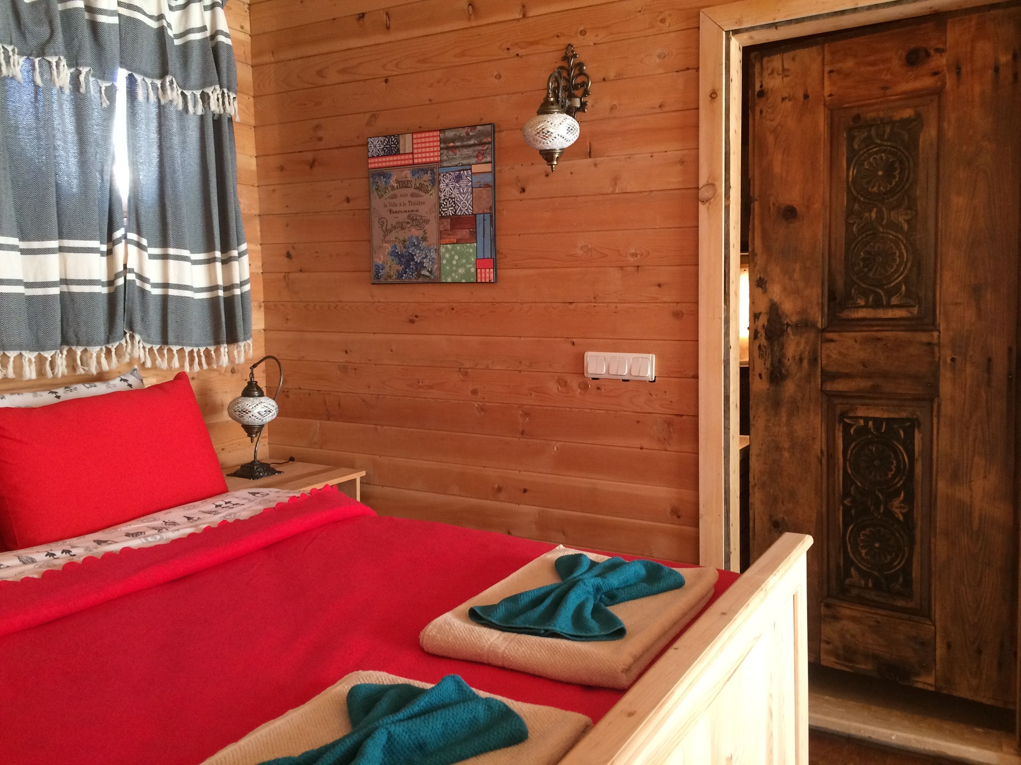 Habitación de cabaña de madera con una cama, una lámpara fijada a la pared y una puerta con intrincados grabados.