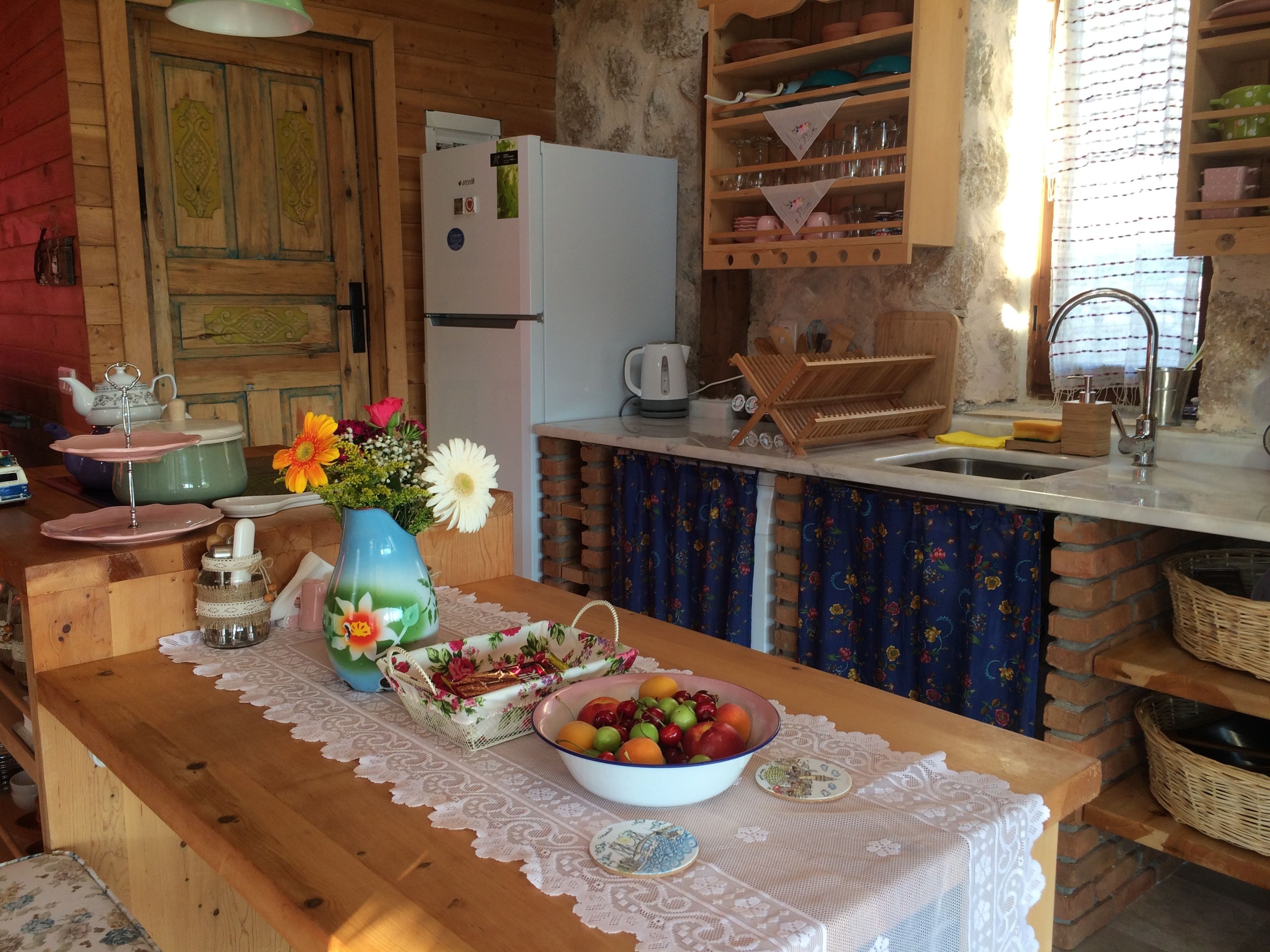 Une cuisine rustique avec des meubles de rangement en bois, un réfrigérateur blanc et un plan de travail en bois surmonté d’une nappe en dentelle.
