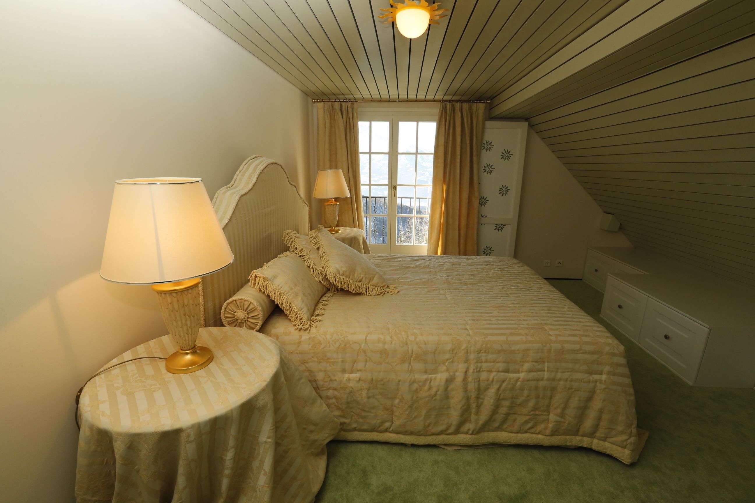 A bedroom with a bed, two bedside tables, a lamp, a dresser, and a window with curtains.