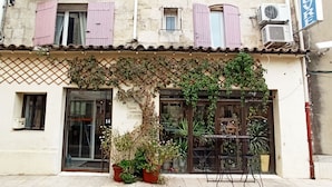Un edificio con puerta de acceso de vidrio, un pequeño espacio al aire libre con mesas y sillas, y un letrero que indica un negocio o centro de servicios.