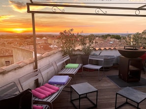 Een terras op het dak met uitzicht op de zonsondergang, voorzien van buitenmeubels, een barbecue en potplanten.