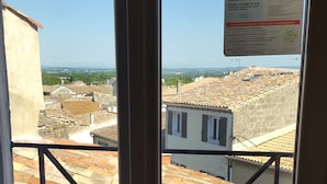 Vista a través de una ventana con baranda de metal, que da a un patio con baldosas de terracota y edificios de arquitectura tradicional.