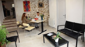Una habitación con pared de piedra, un sofá negro, una mesa de comedor con sillas y una planta en maceta.