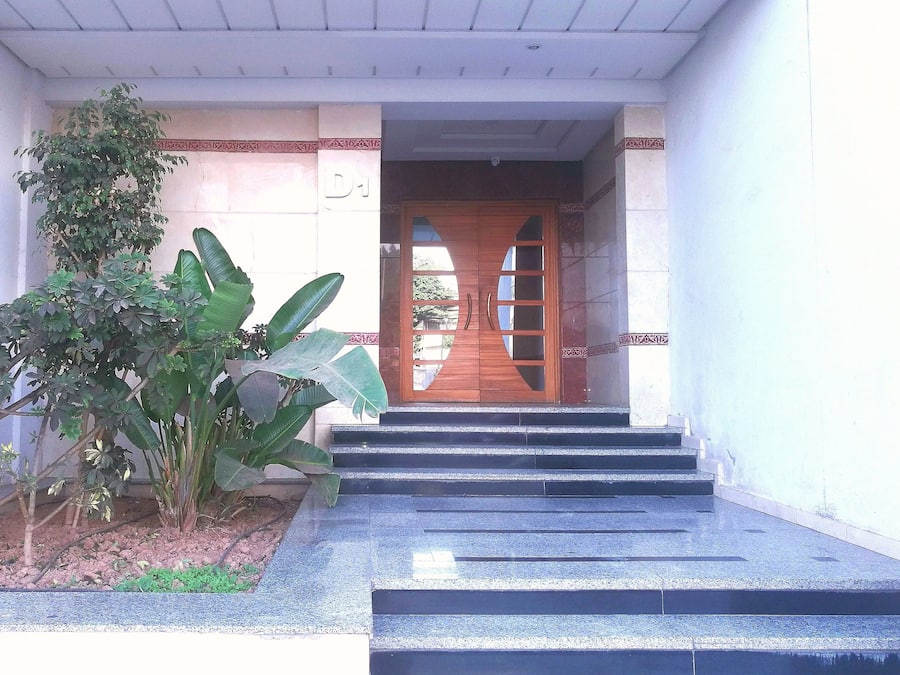 Entrada de prédio com porta de madeira, degraus de acesso e um vaso de planta à esquerda.