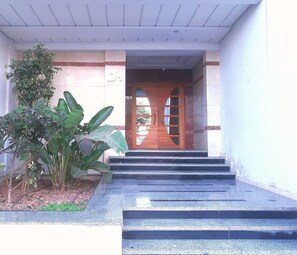 A building entrance with a wooden door, steps leading up to it, and a potted plant to the left. - Residence Tifaouine Agadir (Agadir)