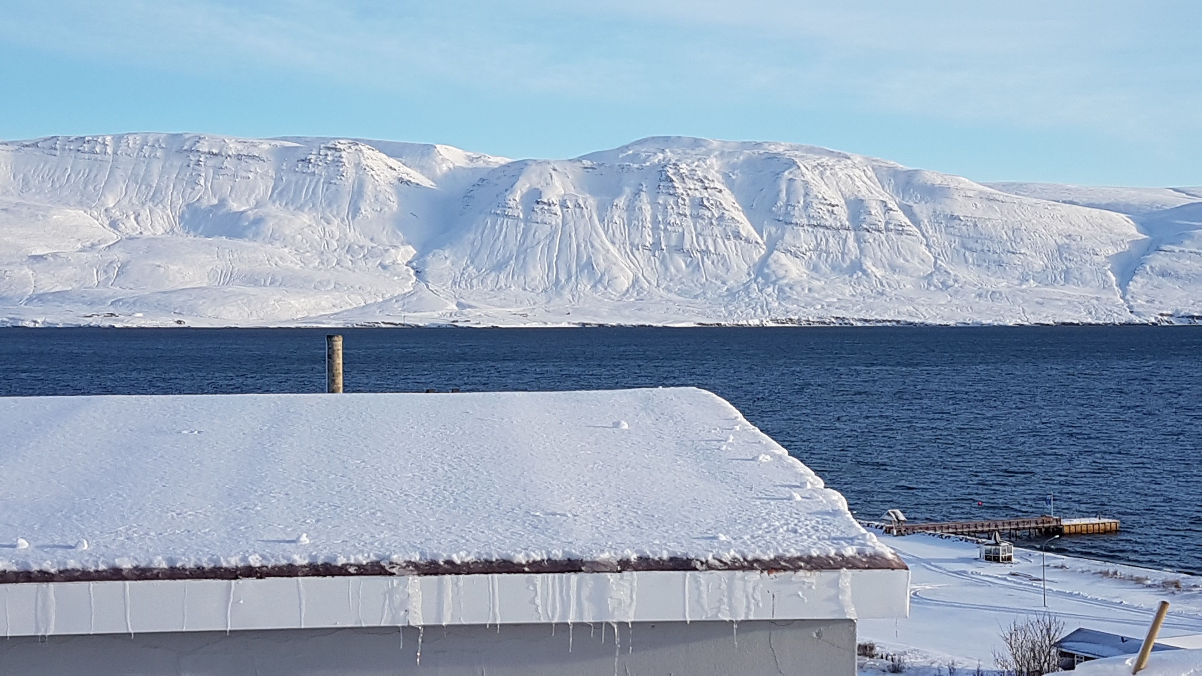 Un paisaje nevado con un extenso glaciar al fondo y un edificio de techo cubierto de nieve en primer plano.