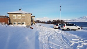Et sneklædt landskab med en bygning, parkerede biler og et flagstang.