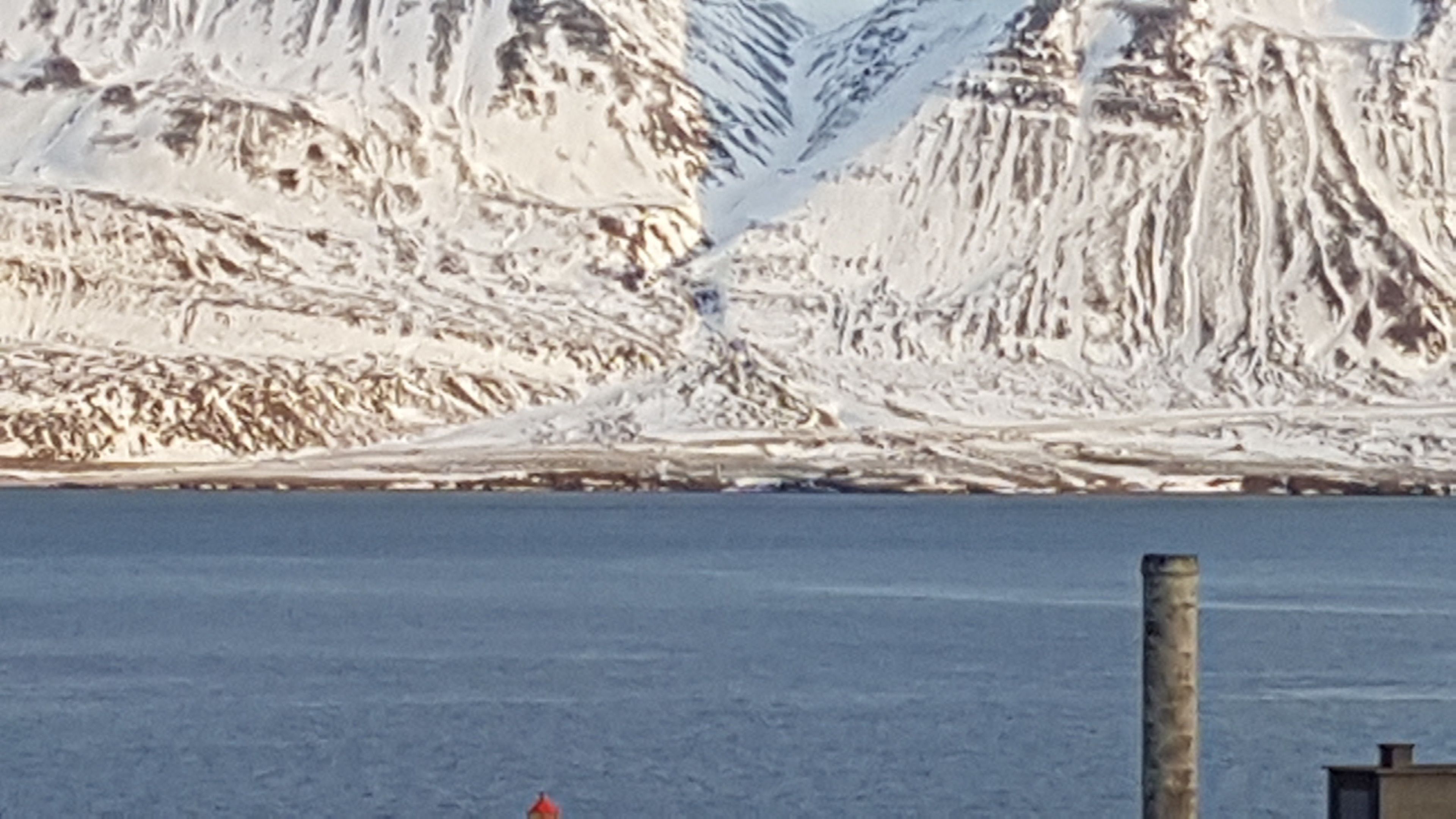 Un paisaje montañoso nevado con una masa de agua al frente.