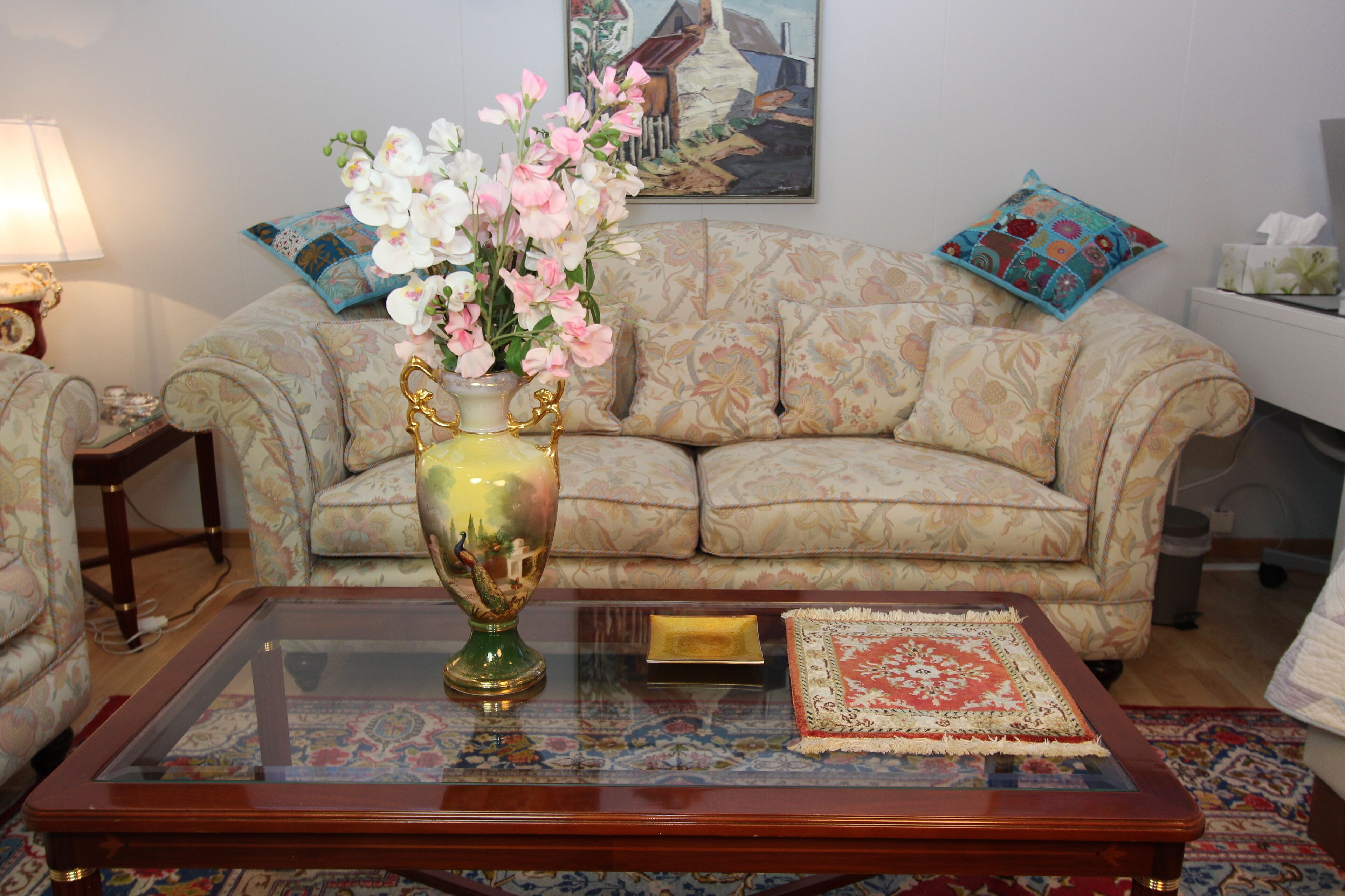 Een woonkamer met een bloemenvaas, een gestreept sofa, een glazen salontafel en een schilderij aan de muur.