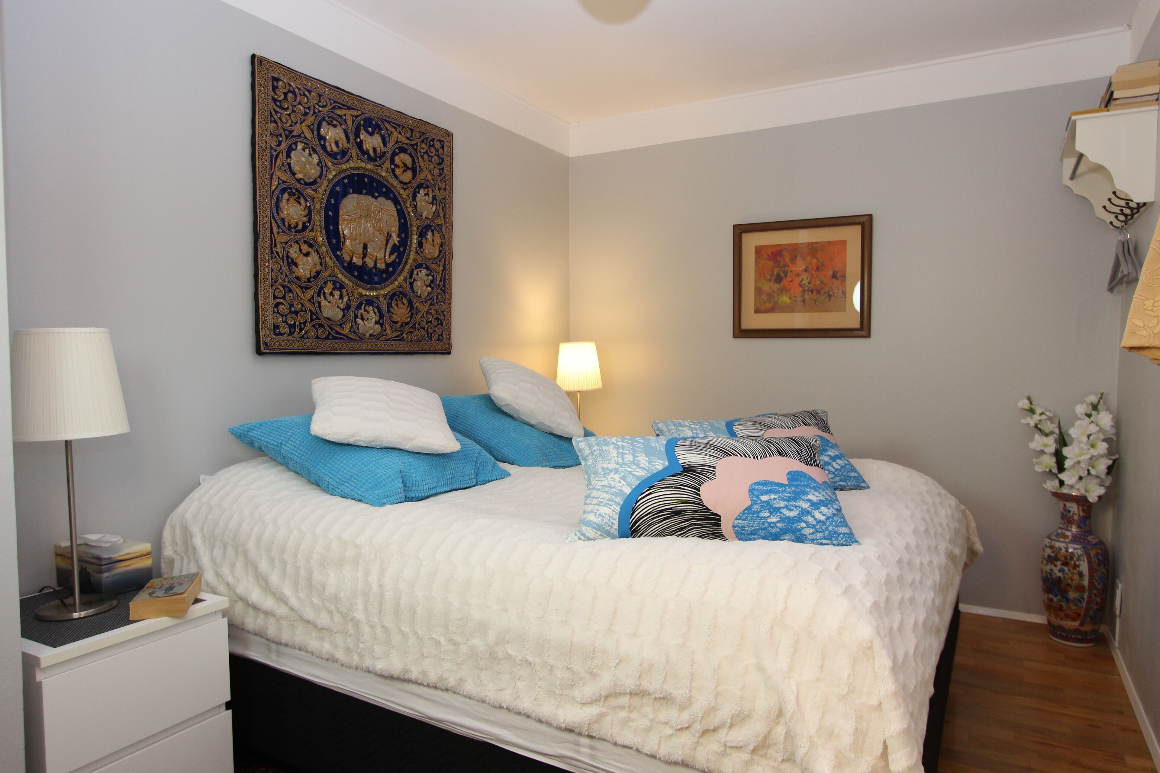 A neatly made bed with a white duvet, blue and white pillows, and a decorative headboard.