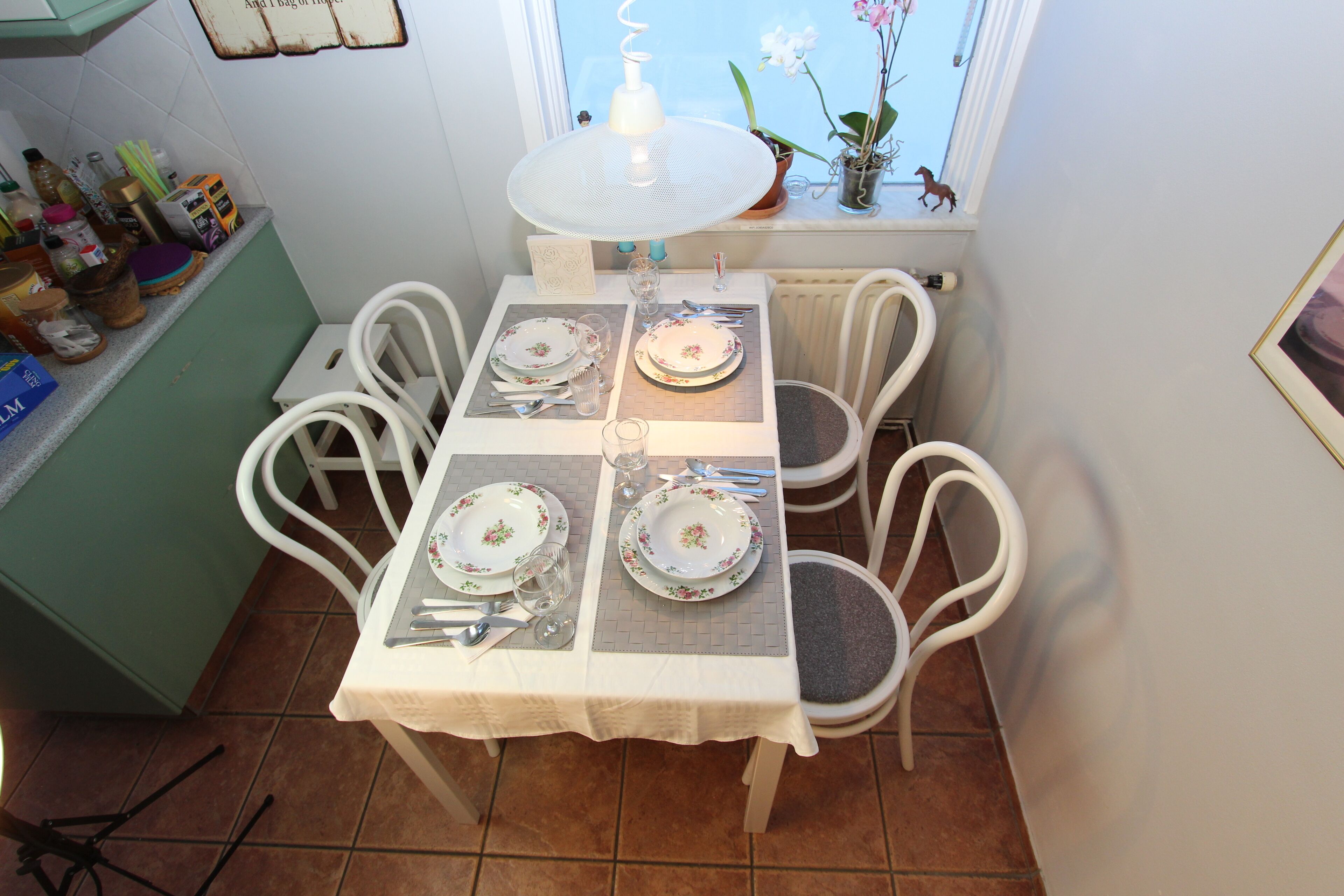 A dining area with a table set for four, surrounded by white chairs.