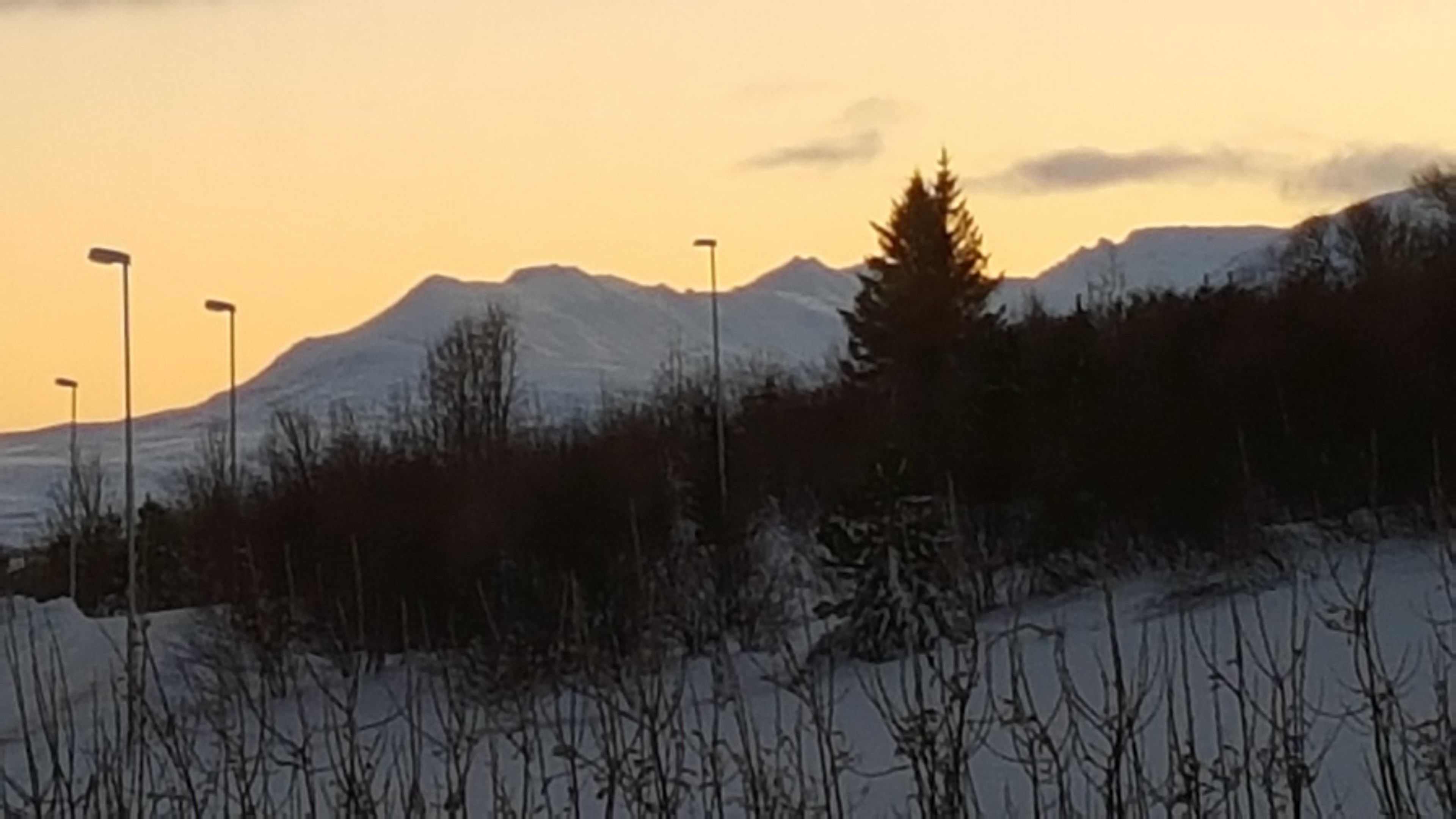 A snowy landscape with a mountain in the background and street lamps in the foreground.