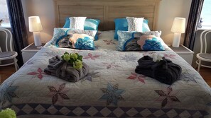 A neatly made bed with a floral quilt, two pillows with a blue and white pattern, and a bedside table with a lamp. - The Viking Country Club (Hjalteyri)