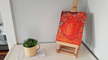 A small wooden easel with a colorful abstract painting, a potted plant, and a beige mug on a doily.