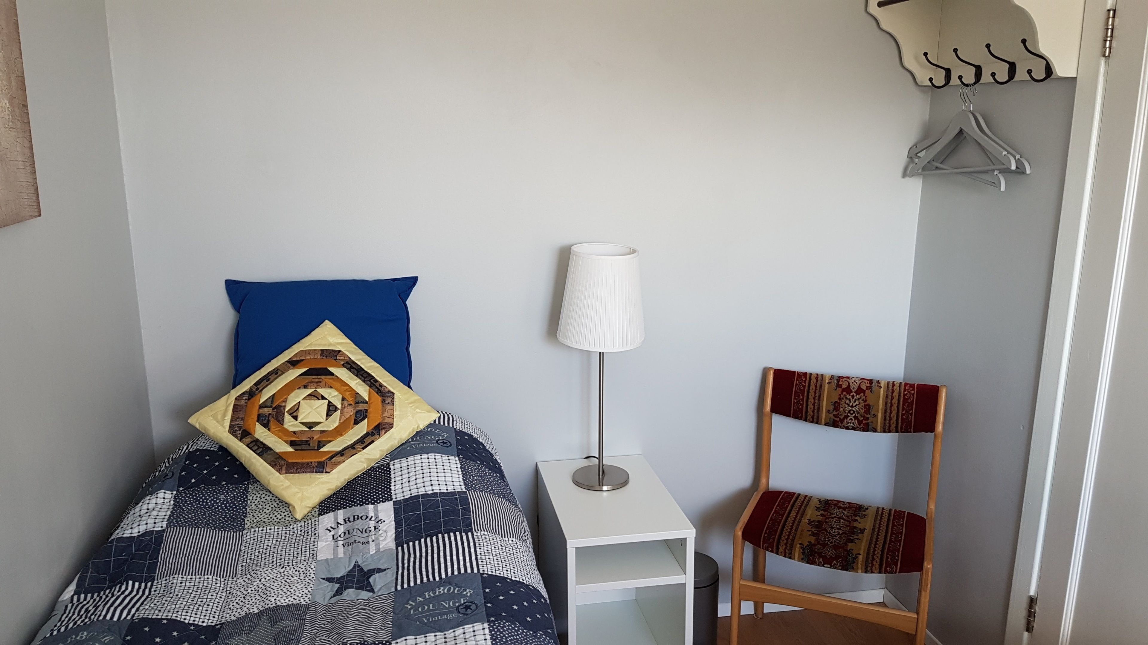 Un dormitorio ordenado con cama, mesita de noche, lámpara y silla.