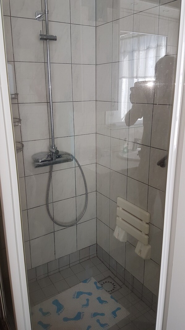 Et lille badeværelse med fliser, en håndbruser og et brusehosesæt.