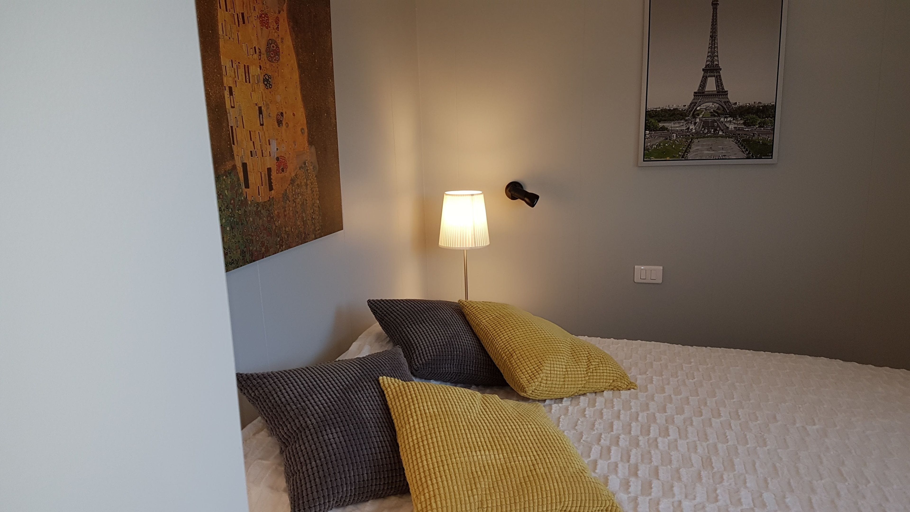 Ett hotellrum med en säng, en lampa, en tavla och en affisch med Eiffeltornet på.