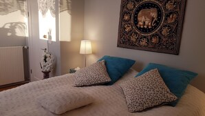 A bedroom with a bed, two pillows, a nightstand, a lamp, a wall decoration, and a window with curtains. - The Viking Country Club (Hjalteyri)