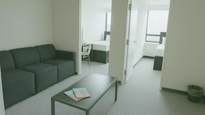 A modern living room with a sofa, a coffee table, and a view into a bedroom through a doorway. - Parkside Student Residence (Toronto)