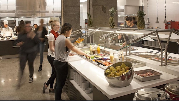 A buffet area with various food items, a chef preparing food, and a counter with condiments. - Parkside Student Residence (Toronto)