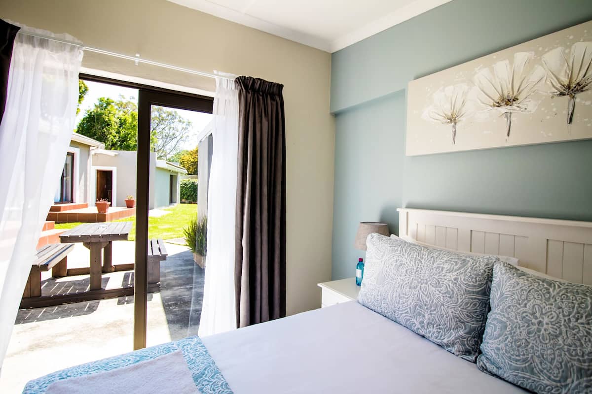 A bedroom with a bed, a nightstand, a lamp, and a view of an outdoor patio with a table and chairs.