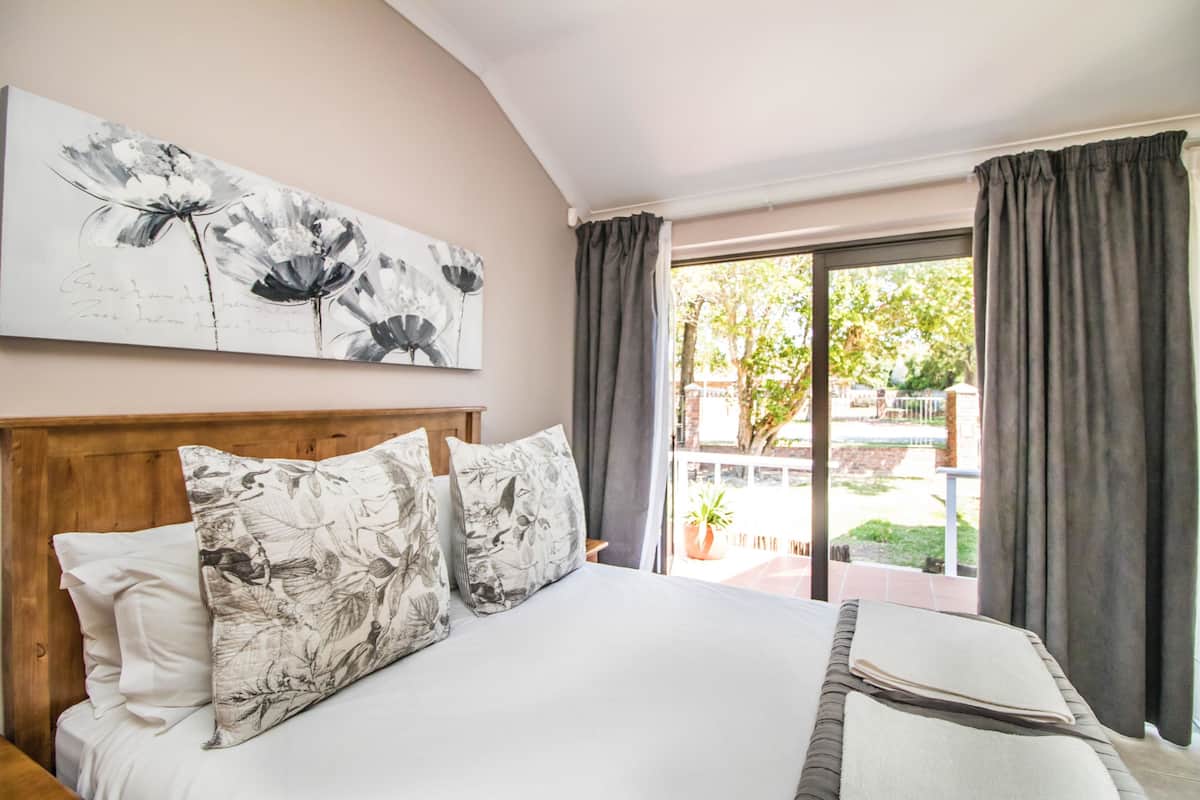 A bedroom with a bed, floral artwork, and a view of the outdoors.
